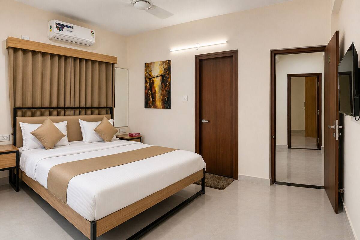 A hotel room with a bed, a TV, a door, and a painting on the wall.