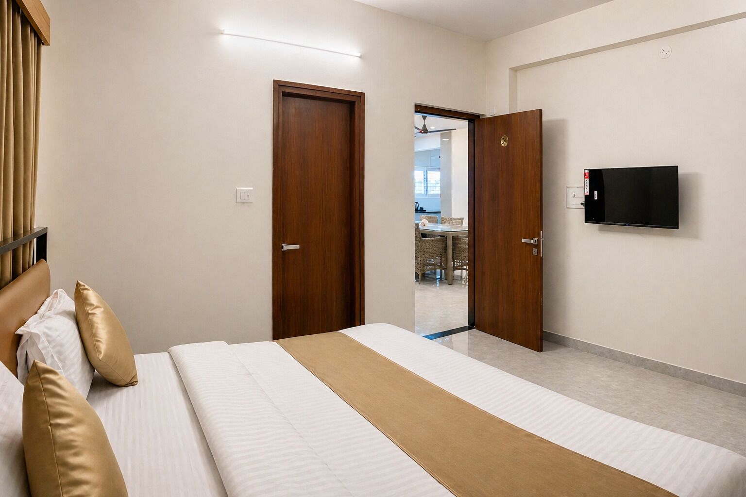 A bedroom with a bed, two doors, a TV, and a view into a dining area.
