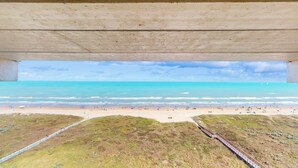 Ein Strand unter einer Betonkonstruktion mit Blick auf das Meer und Strandbesucher.