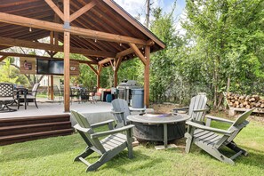 Eine Terrasse im Freien mit Grill, Adirondack-Stühlen und einem Feuerkorb.