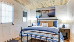 A bedroom with a bed, a nightstand, a wall-mounted lamp, a door, and a window with blinds. - Lake LBJ Home: Putting Green, Pavilion & Fire Pit (Kingsland)