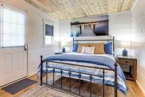 Ein Schlafzimmer mit einem Bett, einem Nachttisch, einer Wandlampe, einer Tür und einem Fenster mit Jalousien.