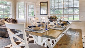 A dining area with a wooden table, white chairs, and a bench. There are windows with blinds, a mirror on the wall, and a door. - Lake LBJ Home: Putting Green, Pavilion & Fire Pit (Kingsland)