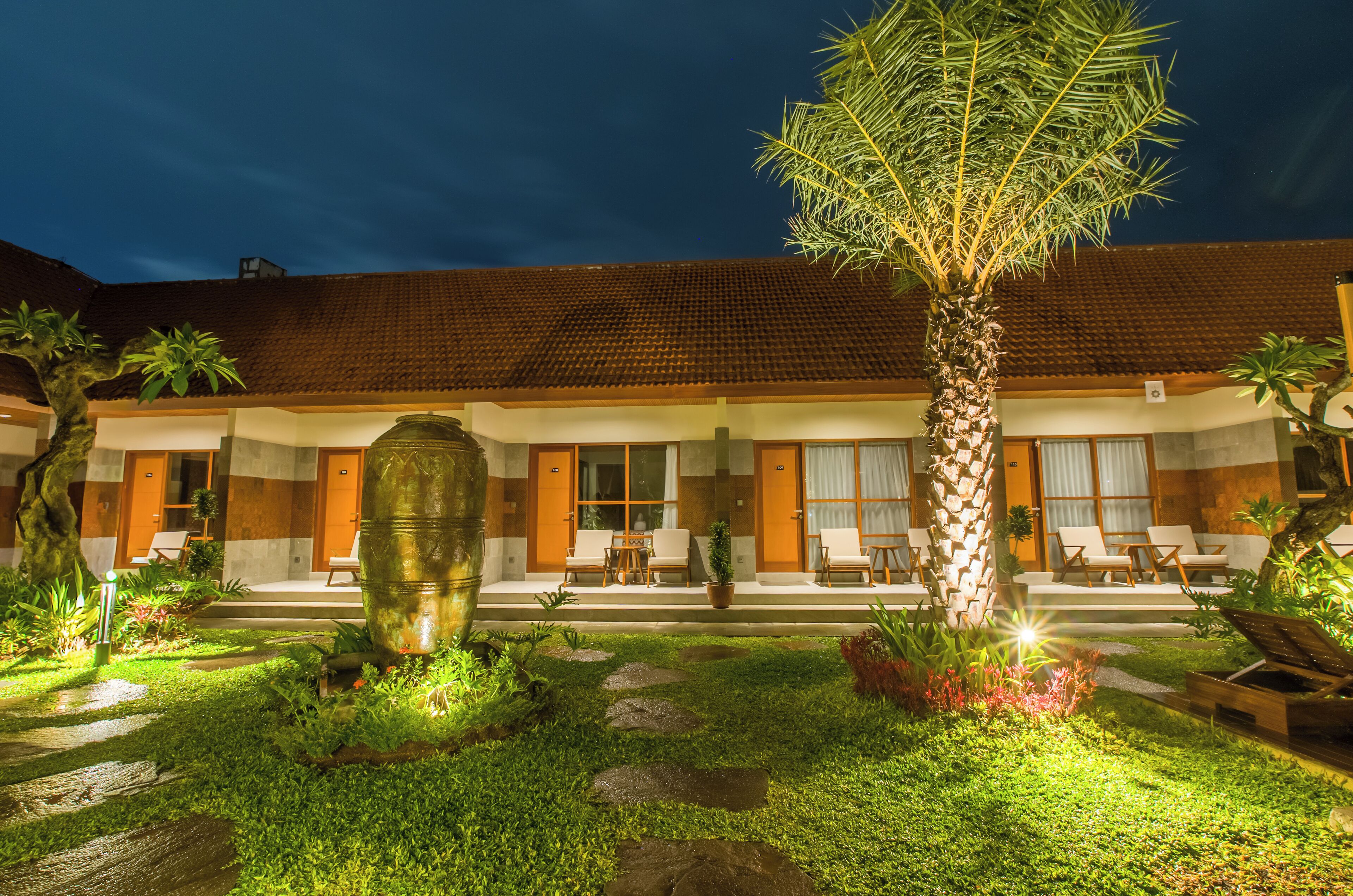 A hotel with a tiled roof, a well-maintained garden with a palm tree, and outdoor seating.