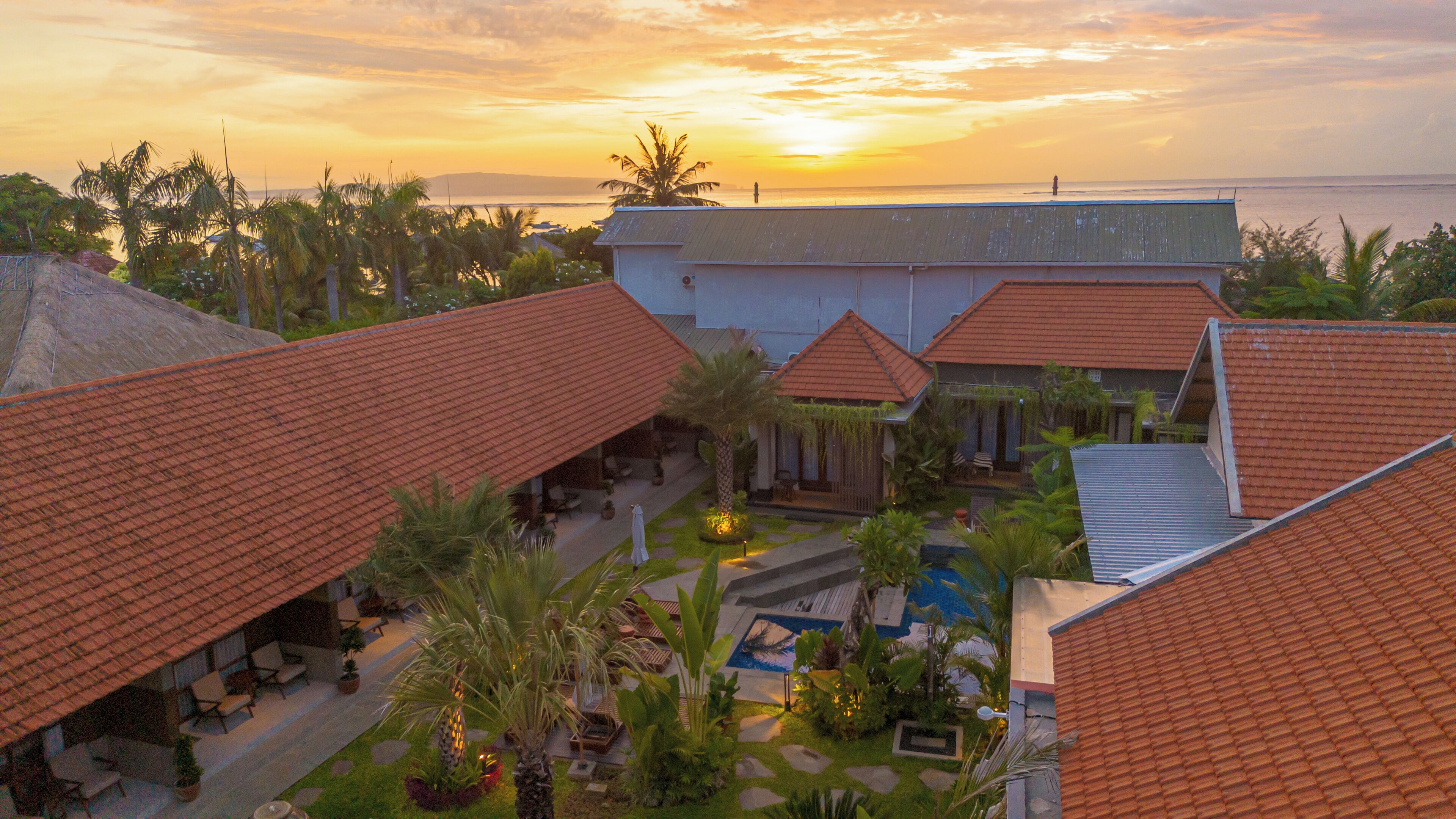 A resort with multiple buildings, a swimming pool, and a view of the ocean at sunset.
