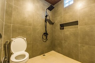 Casa de banho com sanita, chuveiro e um prateleira com produtos de higiene pessoal.