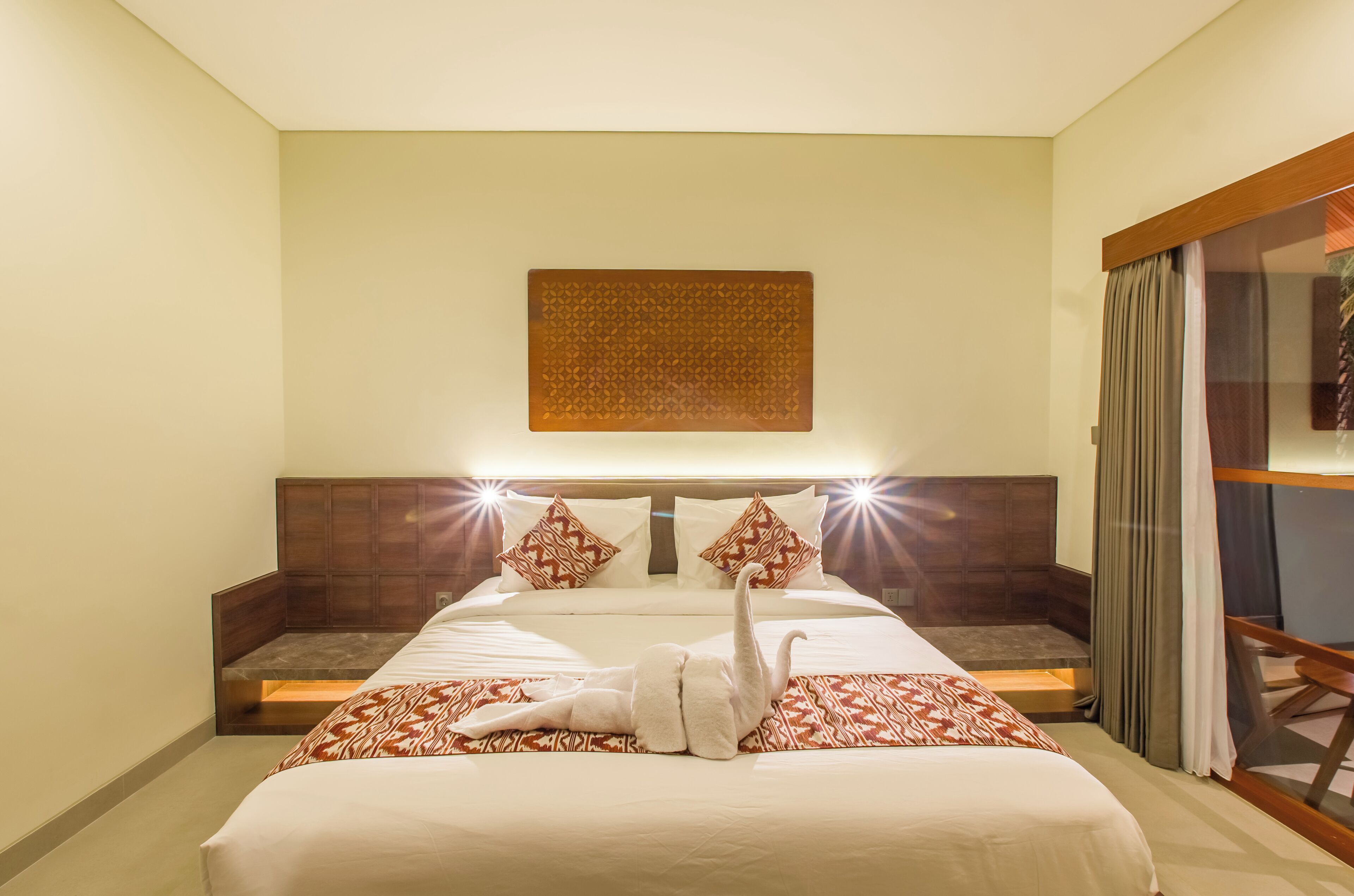 Habitación de hotel con una cama grande, cabecero de madera, una obra de arte en la pared y una zona de estar con vistas.