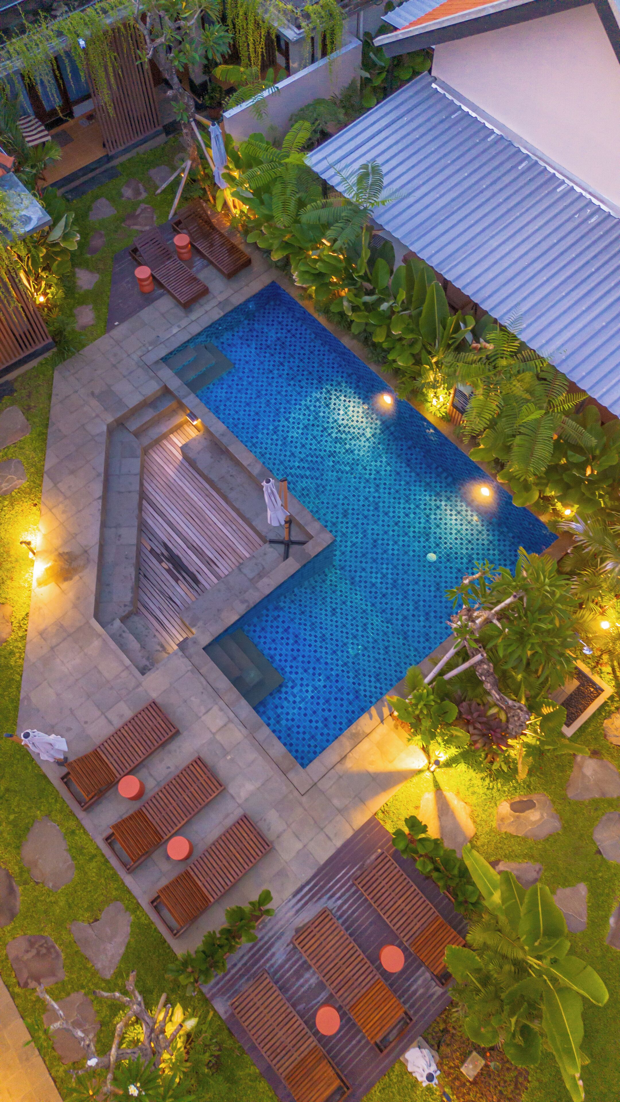 An aerial view of a swimming pool with surrounding lounge areas, a small deck, and tropical plants.