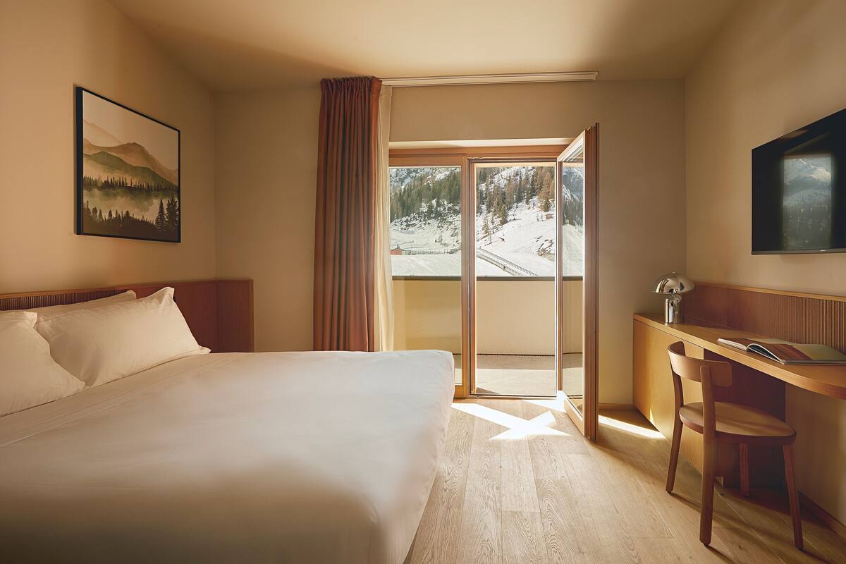 Habitación de hotel con cama, escritorio y vista a un paisaje nevado a través de la ventana.
