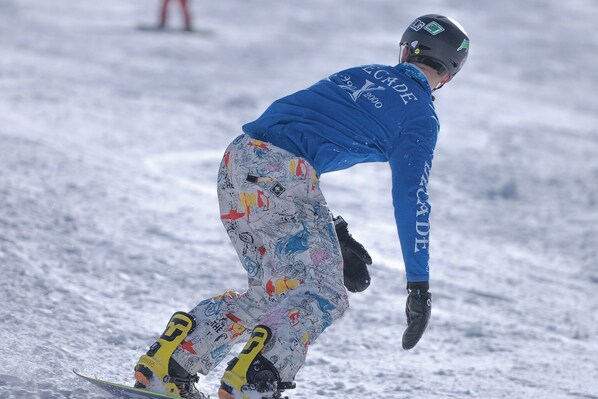 En snowboardåkare i en blå jacka och mönstrade byxor på en snötäckt sluttning.