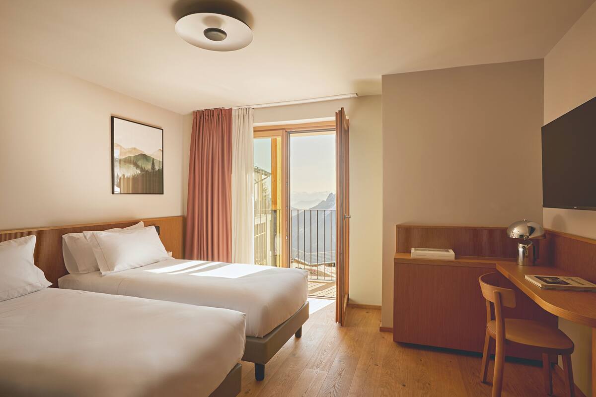 Habitación de hotel con dos camas, un escritorio, una silla, un televisor y un balcón con vistas.
