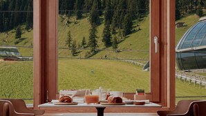 Een eethoek met een gedekte tafel voor twee, met uitzicht op een bergachtig landschap met bomen en een skilift.