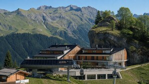 Een modern berglodge met meerdere gebouwen, een skilift en een achtergrond van ruige bergen en beboste hellingen.