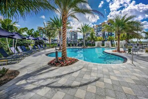 A pool area with lounge chairs, palm trees, and a clear blue sky. - Hard Rock Stadium Home Base! Luxe Condo w/ Pool (Miami Gardens)