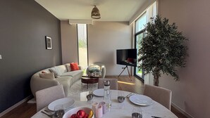 A modern living room with a dining area, a sofa, a TV, and a large plant. - Resort-Style - 4BR Villa, Arabian Ranches 3 (Dubai)