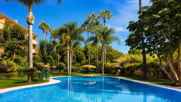 A swimming pool surrounded by palm trees and a building. - Dunas de Cabopino · 2BR Apartment with PRIVATE GARDEN (Marbella)