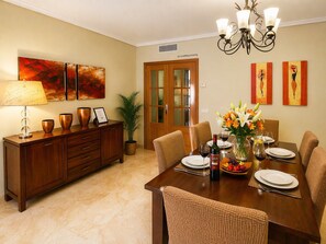 A dining room with a wooden table set for six, a chandelier, and artwork on the walls. - Dunas de Cabopino · 2BR Apartment with PRIVATE GARDEN (Marbella)