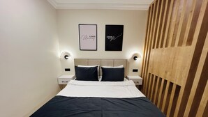 Quarto bem organizado com cama, duas mesas de cabeceira e duas luminárias fixadas na parede.