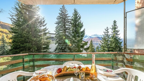 Mesa lista para el desayuno con vista a la montaña, una botella de vino y una cesta de pan.