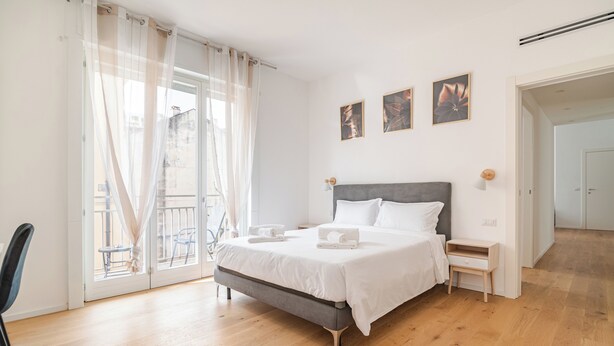 A bedroom with a bed, a nightstand, a chair, and a view through a glass door. - COMO Centro Luxury suites just steps from the lake (Como)