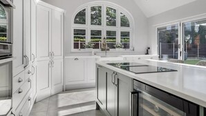 A modern kitchen with white cabinetry, a large island, and a window with a view of greenery. - Luxury Detached House,  Private Grounds. With Hot Tub, Sauna, Pool Table. (Weston)