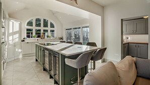 A modern kitchen with a large island, white cabinetry, and a dining area with bar stools. - Luxury Detached House,  Private Grounds. With Hot Tub, Sauna, Pool Table. (Weston)