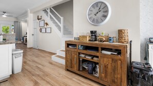 Een ruime keuken met houten vloeren, een grote wandklok en een houten kast vol servies.