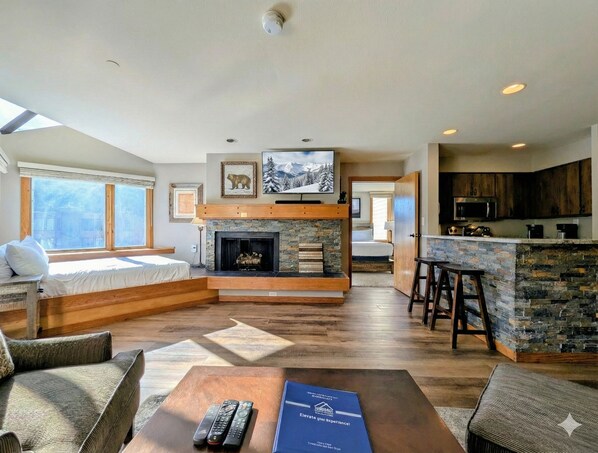 A spacious living area with a fireplace, a kitchen with a stone island, and a large window providing natural light. - Lake Views, Sleeps 6, New Listing! (Keystone)