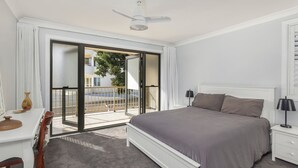 Ein Schlafzimmer mit Bett, Nachttisch, Lampe und Blick auf einen Balkon mit Geländer.