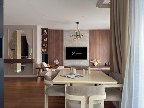 Un espace repas moderne avec une grande table, des chaises confortables, un téléviseur à écran plat fixé au mur et un panneau décoratif.