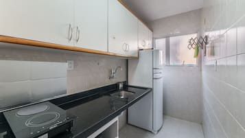 Cozinha com armários brancos, bancada preta, fogão embutido e geladeira.