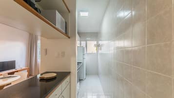 Un couloir étroit, avec un coin cuisine sur la gauche, comprenant un comptoir avec un évier, une télévision et une table à manger. Le couloir a des murs carrelés et un luminaire au plafond.