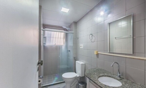 A bathroom with a shower, toilet, sink, and a mirror. - Apt 1 Bedroom in Salvador Ian0104 (Salvador)