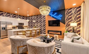 Un salon moderne avec une cheminée, une cuisine en arrière-plan et un néon.