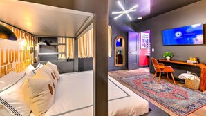Moderni hotellihuone, jossa on suuri sänky, työpöytä tuolilla, televisio ja koristeellinen peili.