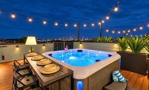 A rooftop hot tub with a city view, string lights, and a table with plates and a lamp. - Lux Nash Party•10 Beds•Hot Tub•Game Room + Pool (Nashville)