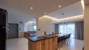 Cozinha moderna com ilha de madeira, sala de jantar com uma mesa comprida e cadeiras, e um espaço de estar com sofá e janela.