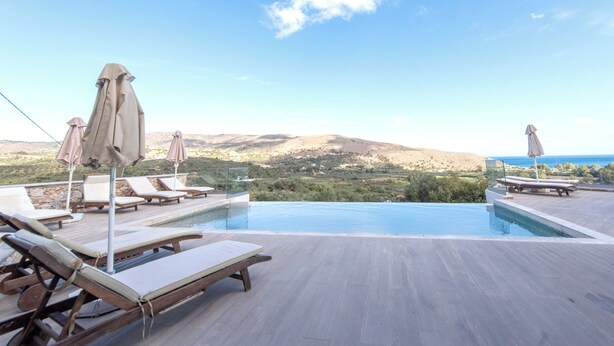Uma piscina infinita com espreguiçadeiras e guarda-sóis, com vista para uma paisagem montanhosa.