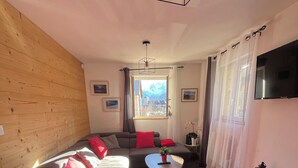Una sala de estar moderna con un sofá, una mesita, una silla, un televisor y un ventanal con vistas a montañas.
