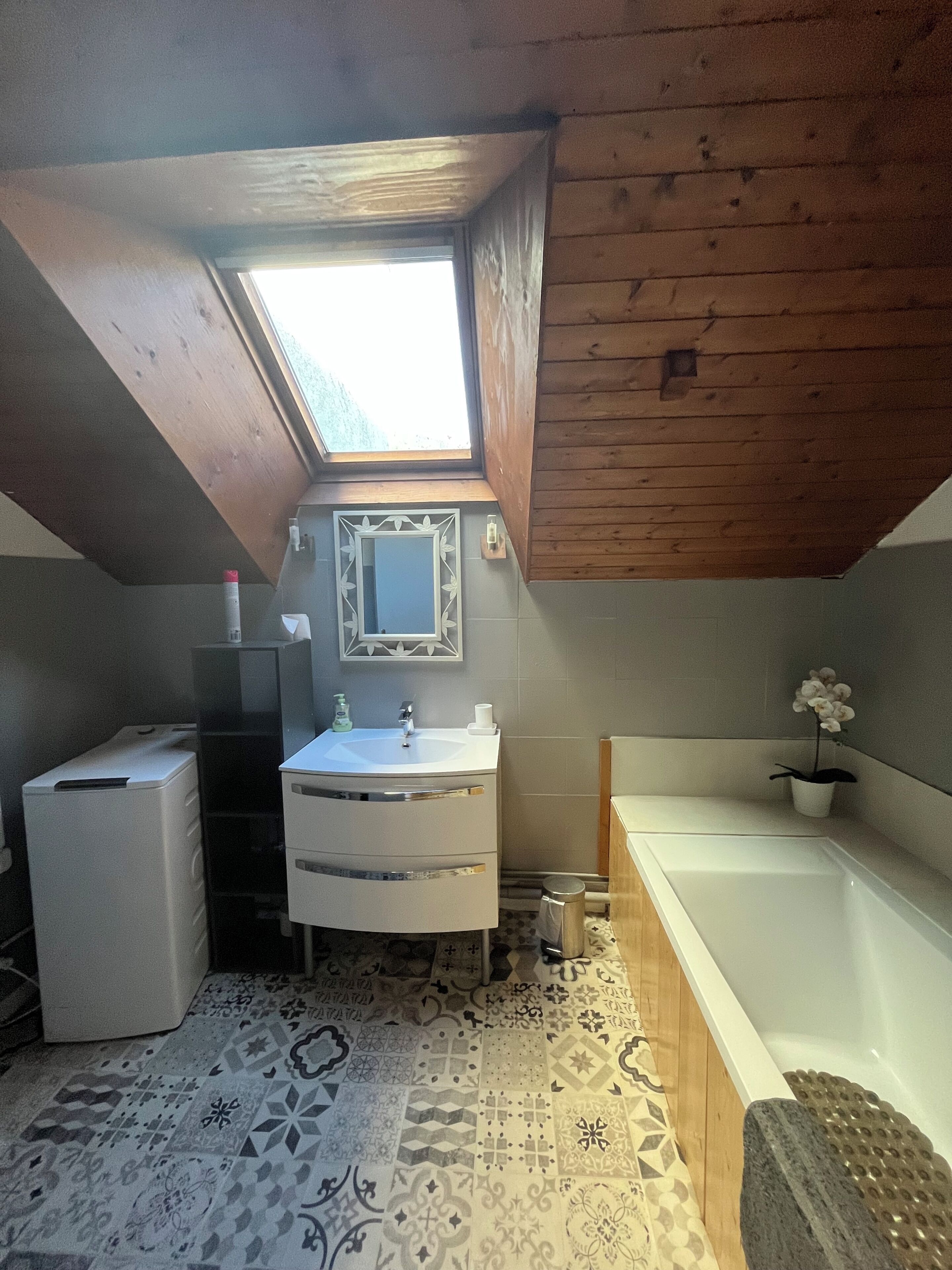 A small, sloped-roofed bathroom with a skylight, a sink, a mirror, a toilet, and a bathtub.