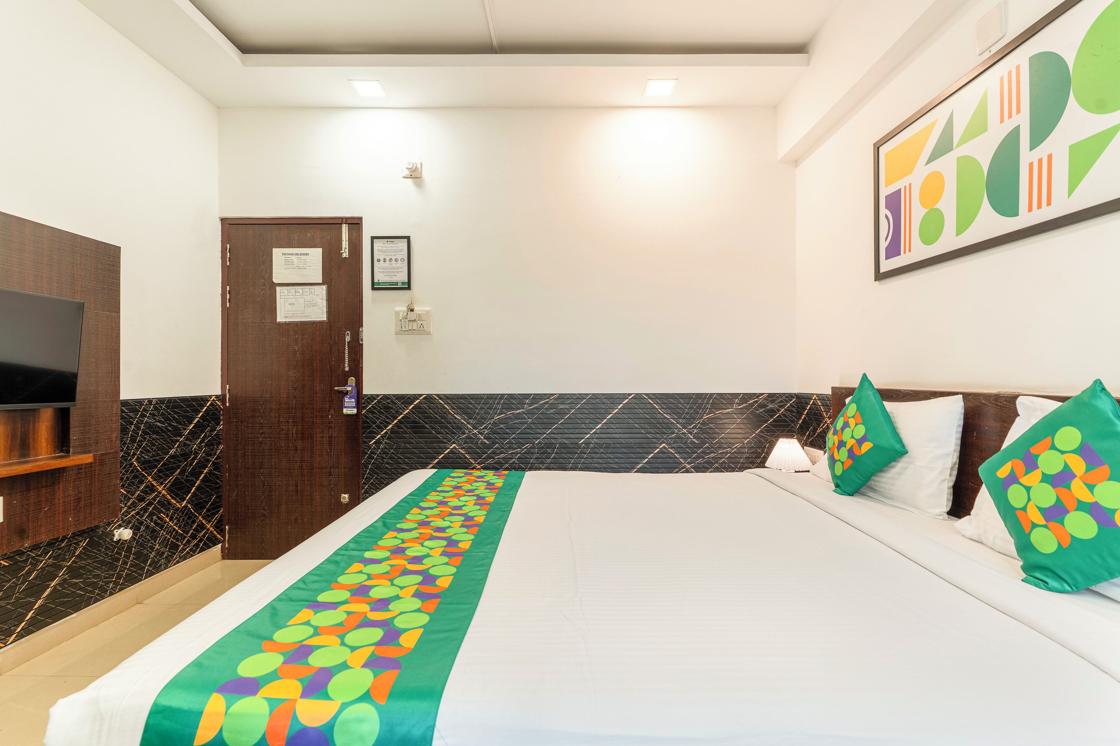A hotel room with a bed, a television, a wooden wardrobe, and a black tiled wall.