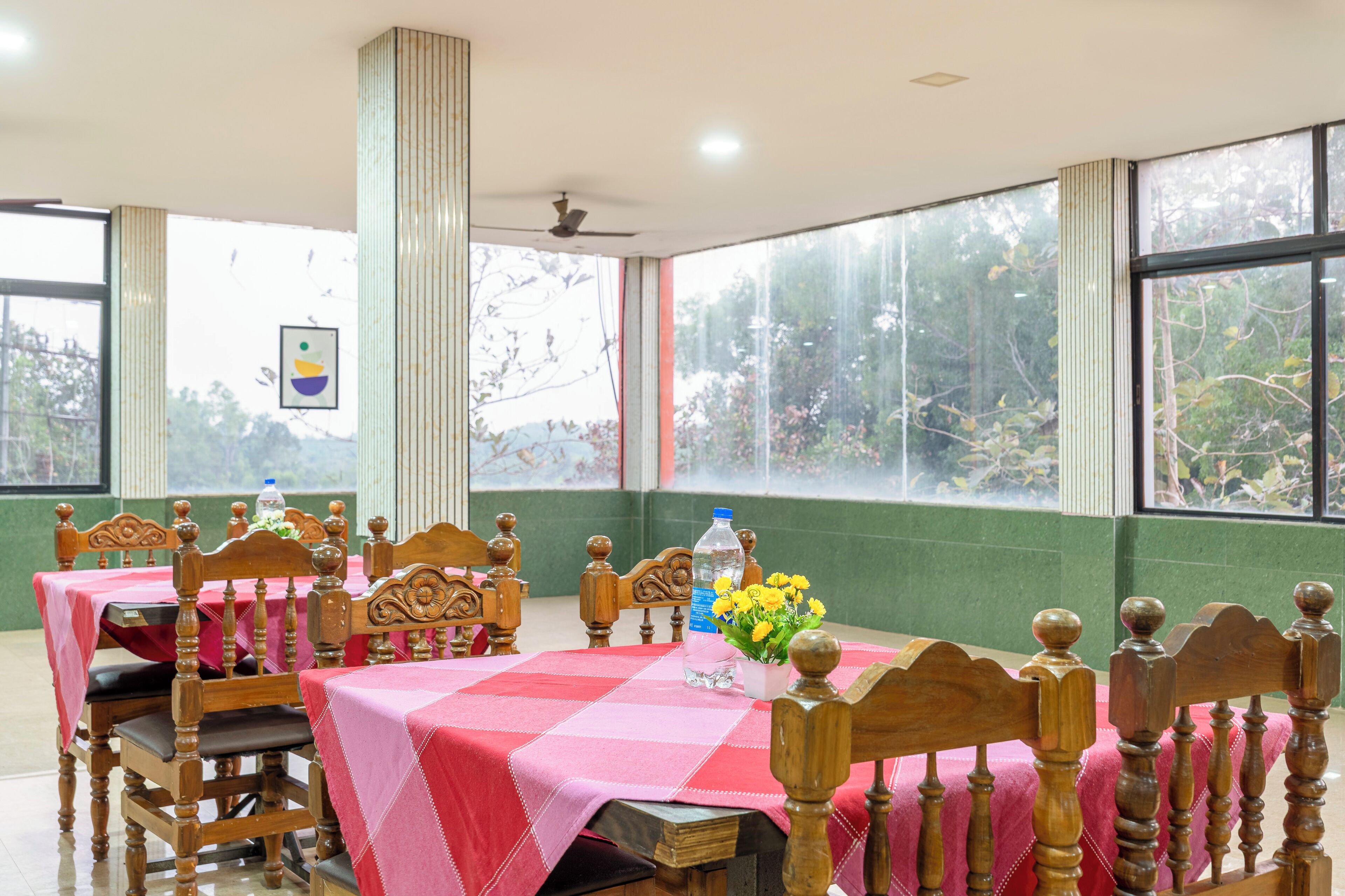 A dining area with wooden chairs and tables, a ceiling fan, and large windows with a view of trees.
