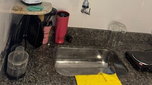 A kitchen counter with a coffee maker, a red mug, a glass, a metal container, and a yellow cloth. - Studio Paris - Downtown Niterói (Niterói)