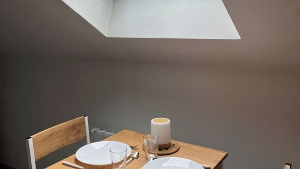 Een eetgedeelte met een tafel gedekt voor twee personen, een kaars en een uitzicht op de lucht door een dakraam.