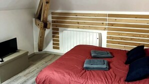 Een slaapkamer met een houten hoofdbord, een rode spreideken en een televisie op een standaard.