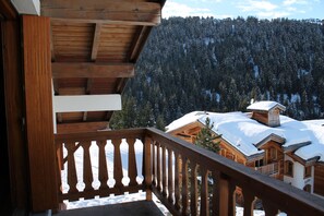 A wooden balcony with a view of a snow-covered mountain and a wooden cabin. - Apartment in the Courchevel Moriond 1650 Chalet (Courchevel)