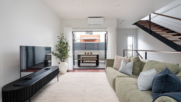 A modern living room with a flat-screen TV, a large potted plant, a wooden bench, and a staircase leading to an upper level. - Copperstone Corner, Richmond (Richmond)