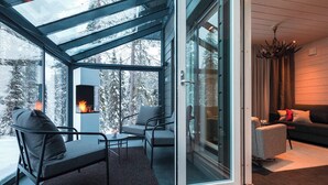A modern interior with a glass door leading to a snowy outdoor area, a fireplace, and a cozy seating area. - Parkside Pyhä (Pelkosenniemi)