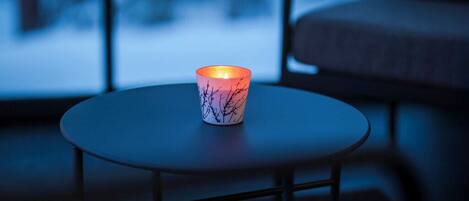 A candle on a round table in a dimly lit room with a view of a snowy landscape through a window.