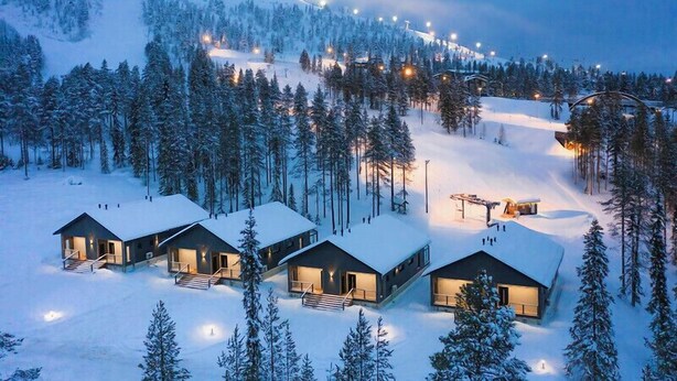 A snow-covered landscape with three cabins, each with a balcony and a staircase leading to the entrance. - Parkside Pyhä (Pelkosenniemi)